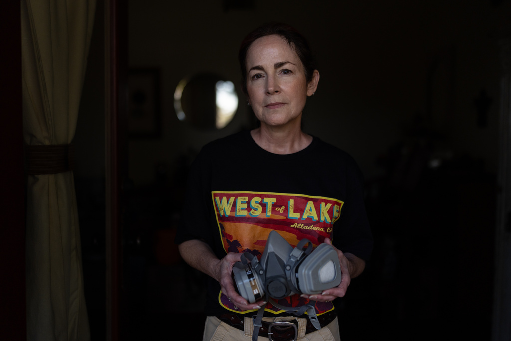 Nina Malone, whose home survived the Eaton Fire, stands for a photo with a respirator she uses when cleaning fire debris inside her home, Dec. 11, 2025, in Altadena, Calif. (AP Photo/Jae C. Hong)