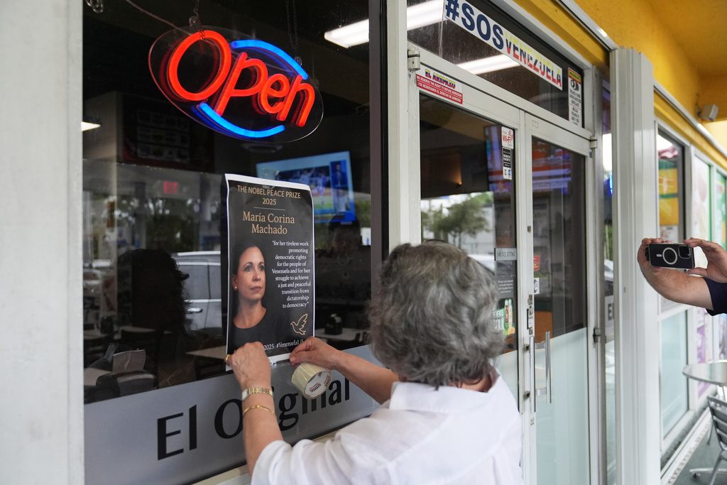 Iris Wilthew hangs a poster in support of Venezuelan opposition leader Maria Corina Machado winning the Nobel Peace Prize, Friday, Oct. 10, 2025, in Doral, Fla. (AP Photo/Lynne Sladky)