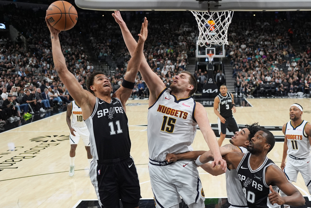 San Antonio Spurs forward Carter Bryant (11) drives to the basket against Denver Nuggets center Nikola Jokic (15) during the first half of an NBA basketball game in San Antonio, Thursday, March 12, 2026. (AP Photo/Eric Gay)
