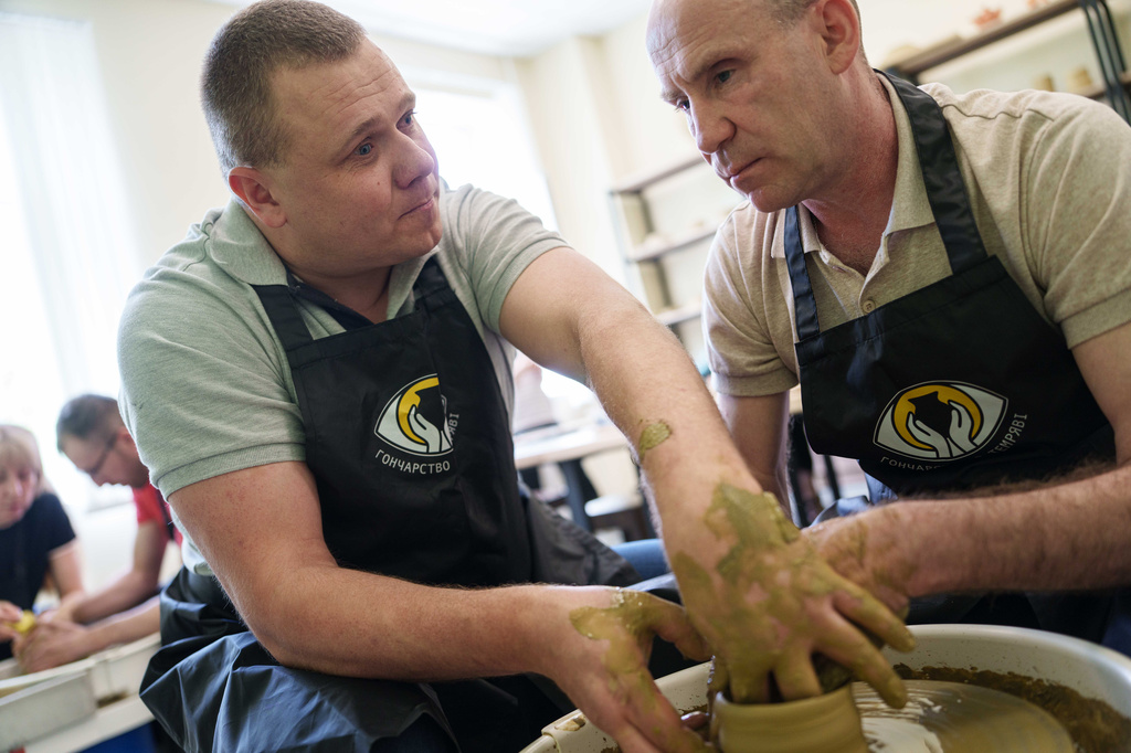 Ivan Shostak, left, a blind Ukrainian war veteran trains his blind comrade Viacheslav Sadovskyi, right, to make a clay plate on a pottery wheel in a workshop at a rehabilitation center in Vinnytsia, Ukraine, on May 21, 2026. (AP Photo/Evgeniy Maloletka)