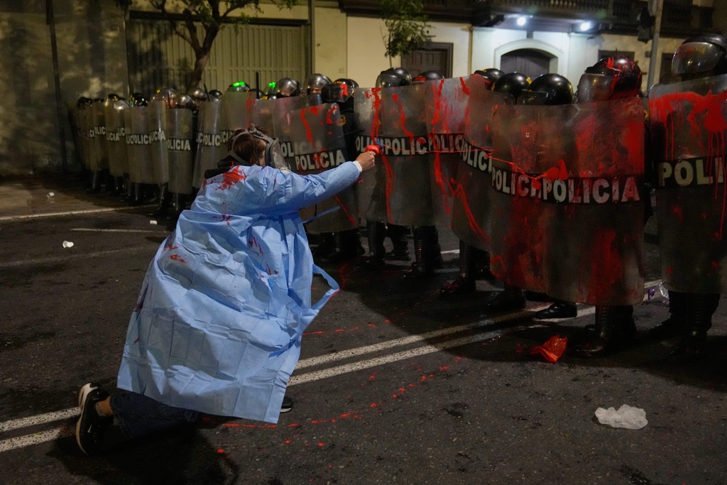 A demonstrator sprays riot police with red paint near Congress during a protest against new President Jose Jeri in Lima, Peru, Wednesday, Oct. 15, 2025. (AP Photo/Martin Mejia)