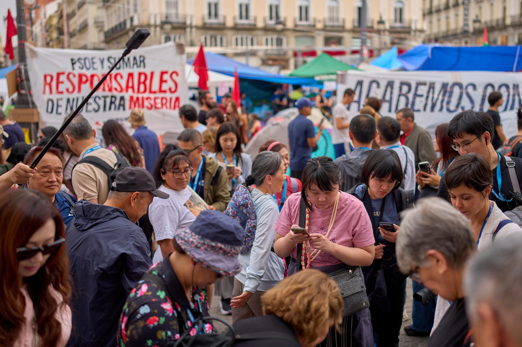 Tourists gather in front of protesters camping during a protest at Sol Square following the eviction last Wednesday of 87-year-old Maricarmen as they demand stronger laws to protect renters in Madrid, Spain, Monday, Sept. 28, 2026. (AP Photo/Manu Fernandez)