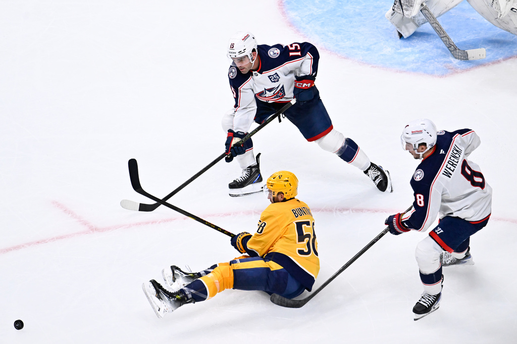Nashville Predators left wing Michael Bunting (58) dishes the puck as Columbus Blue Jackets defenseman Dante Fabbro (15) and defenseman Zach Werenski (8) defend during the third period of an NHL hockey game Thursday, Oct. 9, 2025, in Nashville, Tenn. (AP Photo/John Amis)