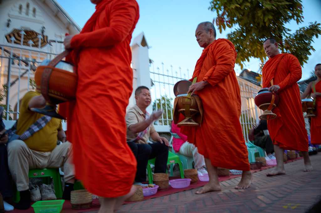Buddhist monks walk in a line seeking alms from residents and tourists waiting along a street in Luang Prabang, Laos, Friday, Nov. 7, 2025. (AP Photo/Eugene Hoshiko)