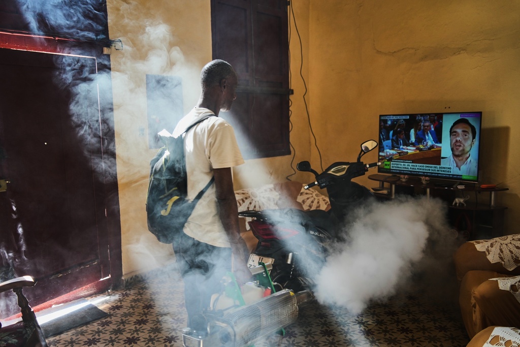 A mosquito control worker fumigates a home where a television plays a government television news report concerning the U.S. forces' capture of Venezuelan President Nicolas Maduro and his wife, in Old Havana, Cuba, Tuesday, Jan. 6, 2026. (AP Photo/Ramon Espinosa)