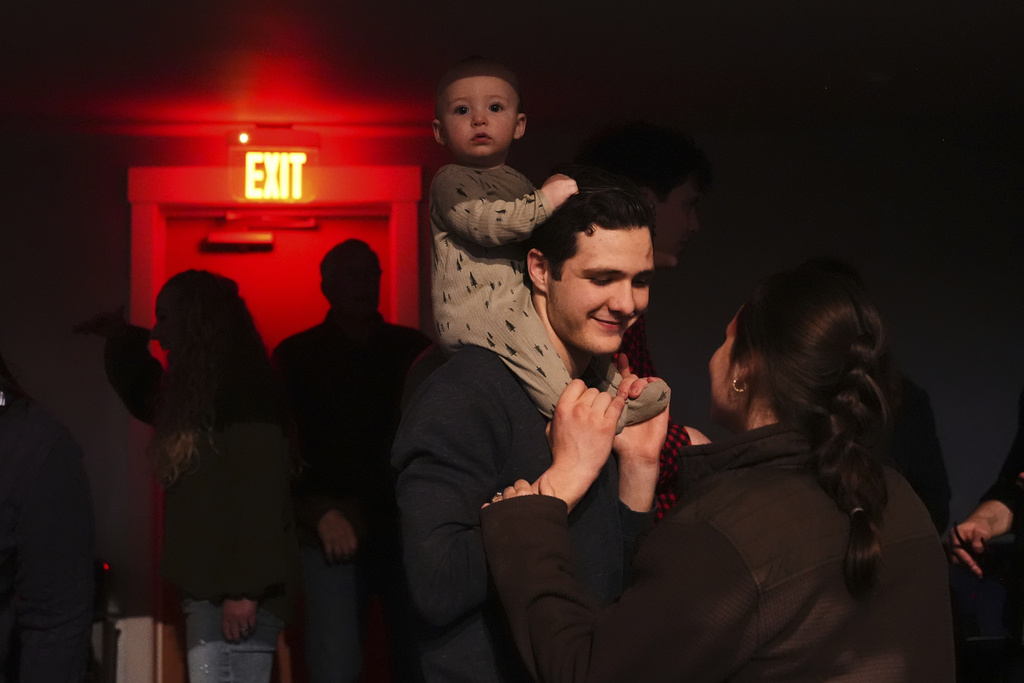 Elijah Mooring, whose family attends King's Cross, an offshoot church from Christ Church, holds son Gideon, 9 months, while talking to wife Evangeline as they wait for a performance from Pastor Doug Wilson and the Dads Band, Friday, April 4, 2025, at the Nuart Theatre in Moscow, Idaho. (AP Photo/Lindsey Wasson)