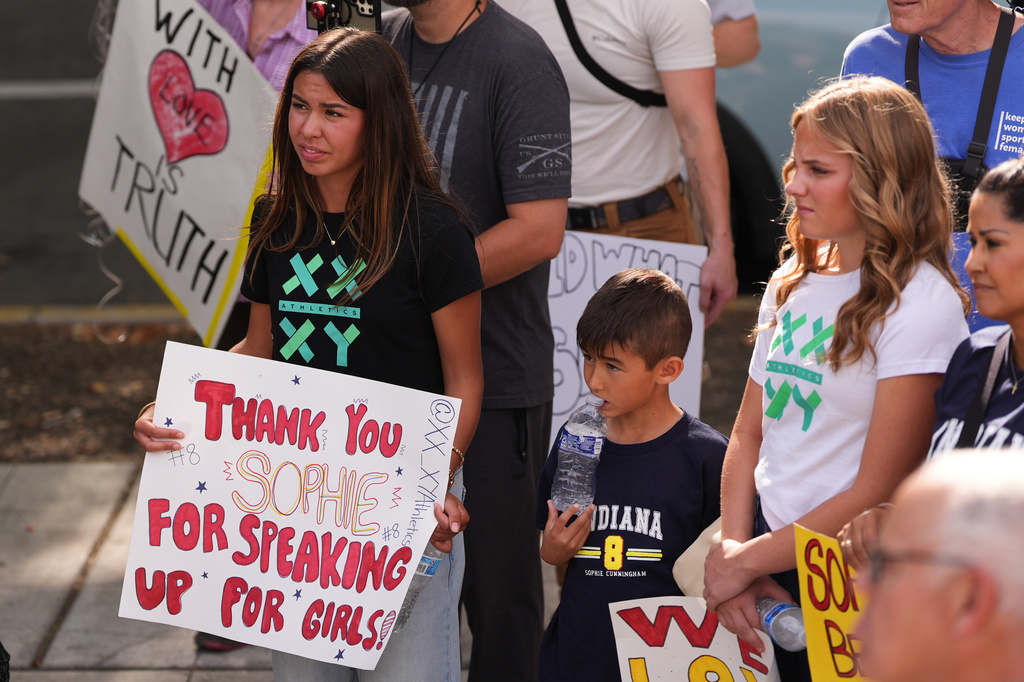 Ahnaleigh Wilson, 17, a track athlete who says she has competed against and placed behind transgender athletes at meets, holds a sign for Indiana Fever guard Sophie Cunningham during a rally before a WNBA basketball game between the Fever and the Seattle Storm, Tuesday, July 28, 2026, in Seattle. (AP Photo/Lindsey Wasson)