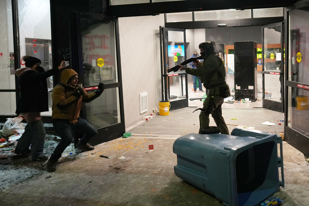 A federal agent points a weapon at a person outside a hotel during a noise demonstration protest in response to federal immigration enforcement operations in the city Sunday, Jan. 25, 2026, in Minneapolis. (AP Photo/Adam Gray)