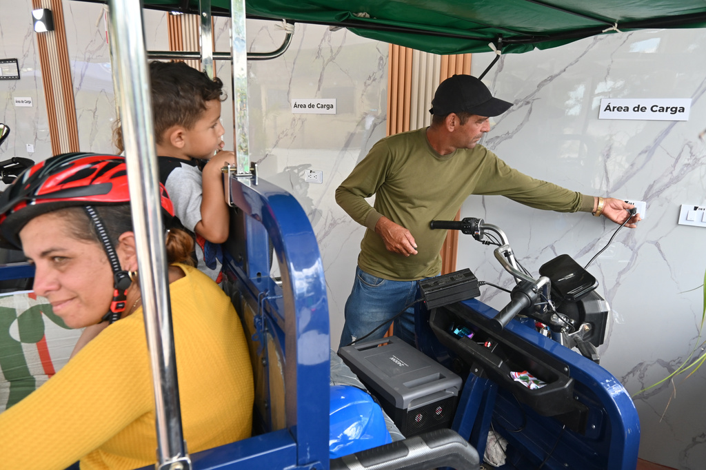 Lorenzo Ravelo, right, plugs in his electric tricycle at a charging station in Santa Clara, Cuba, Saturday, May 2, 2026. (AP Photo/Jorge Luis Banos)