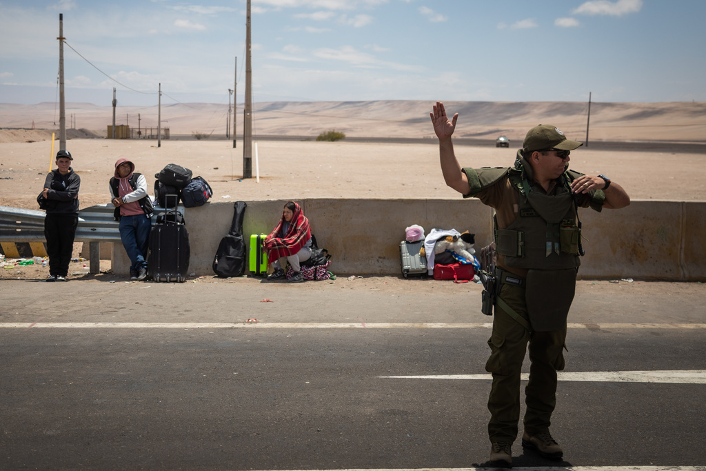 A police officer directs traffic at the Chacalluta border crossing point in Arica, Chile, Friday, Nov. 28, 2025, as migrants mostly from Venezuela wait to cross into Peru. (AP Photo/Ibar Silva)