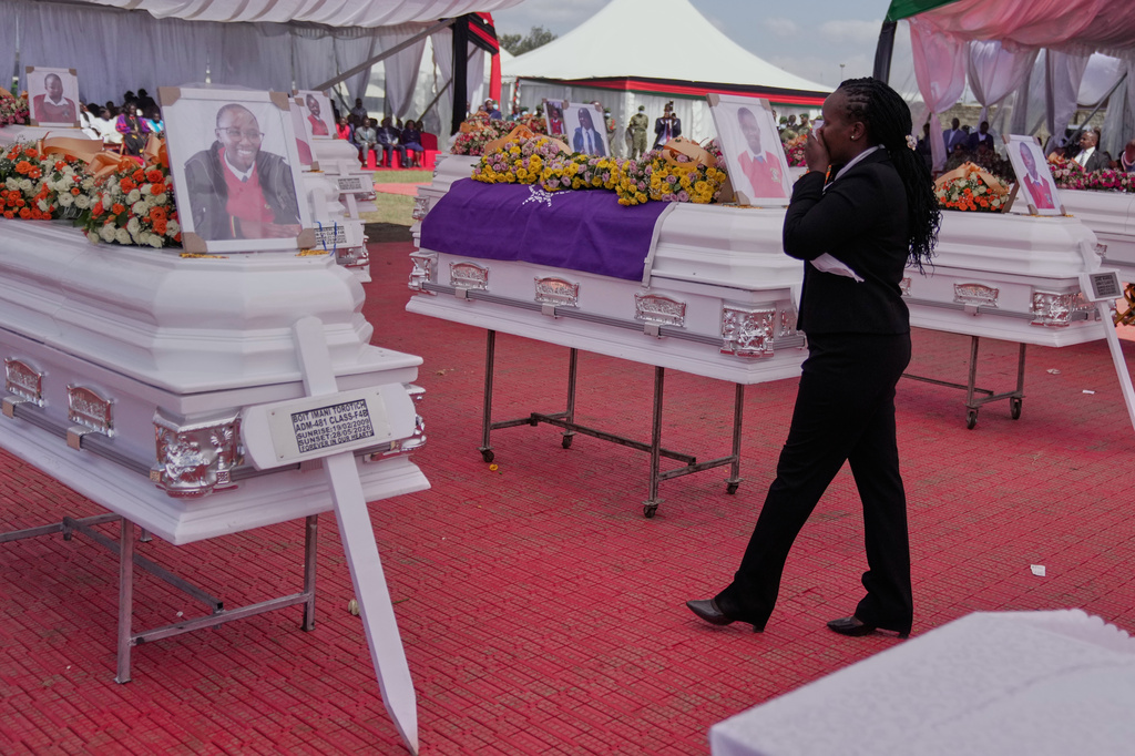 A mourner reacts as she stands between caskets carrying the remains of the 16 girls who died in the Utumishi Academy school fire during a memorial service at Gilgil Stadium, Nakuru County, Kenya, Friday, June 12, 2026. (AP Photo/Brian Inganga)