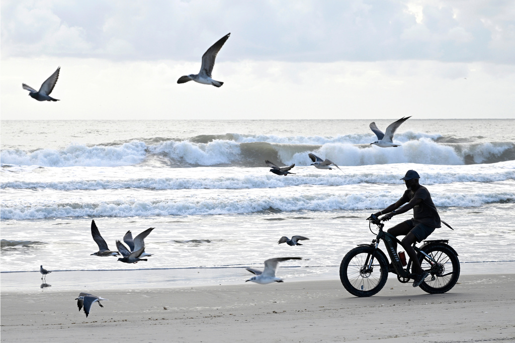 A bicyclist rides along the beach with seagulls as Tropical Storm Imelda kicks up the surf, Monday, Sept. 29, 2025, in Cocoa Beach, Fla. (AP Photo/Phelan M. Ebenhack)