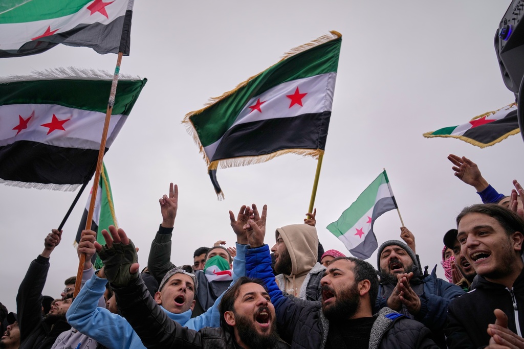 People celebrate and wave Syrian flags as they wait for a parade by the new Syrian army marking the first anniversary of the ousting of the Bashar Assad regime in Damascus, Syria, Monday, Dec. 8, 2025. (AP Photo/Hussein Malla)