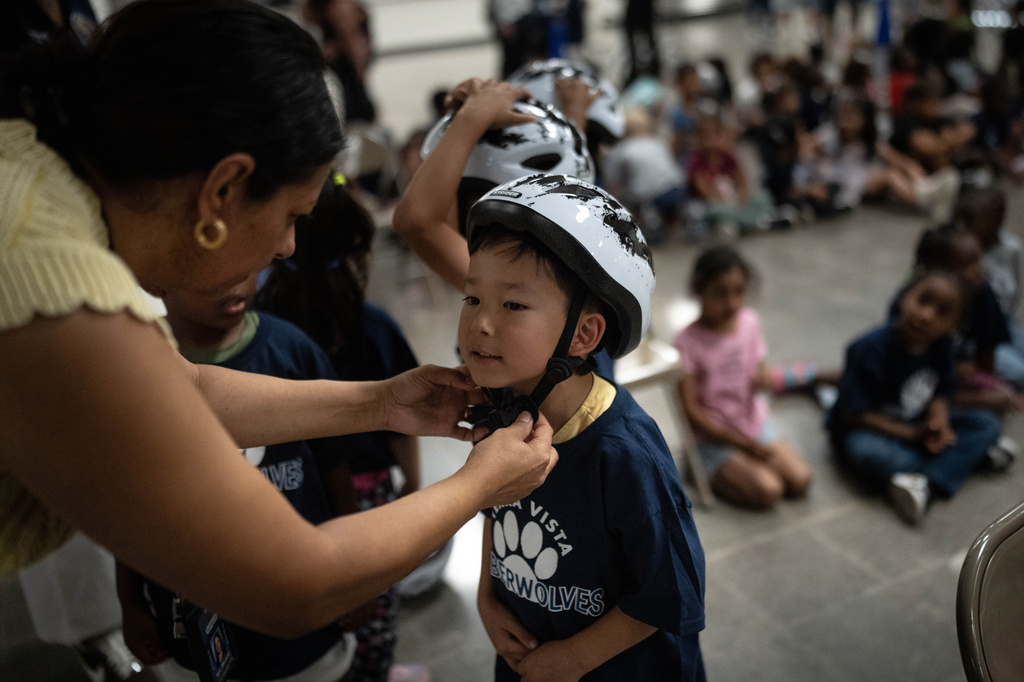 Teachers help students put on their helmets during a learn-to-ride program at Terra Vista Elementary School in Rancho Cucamonga, Calif., Wednesday, Sept. 2, 2026. (AP Photo/Jae C. Hong)