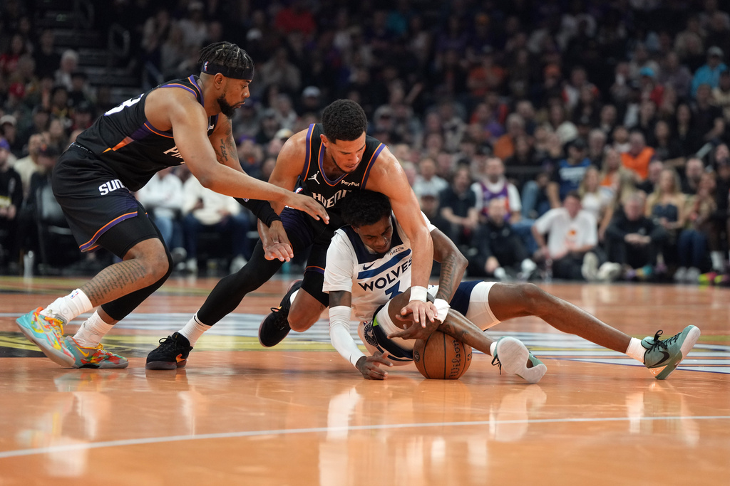 Phoenix Suns guards Jordan Goodwin, left, and Devin Booker, top right, fight for the ball with Minnesota Timberwolves forward Jaden McDaniels, bottom right, during the first half of an NBA basketball game, Friday, Nov. 21, 2025, in Phoenix. (AP Photo/Rick Scuteri)