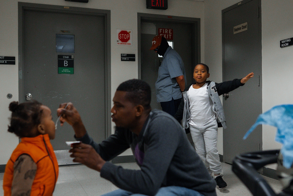 A federal agent waits outside an immigration courtroom as a respondent feeds his child while his other child plays nearby, Thursday, Oct. 2, 2025, in New York. (AP Photo/Olga Fedorova)