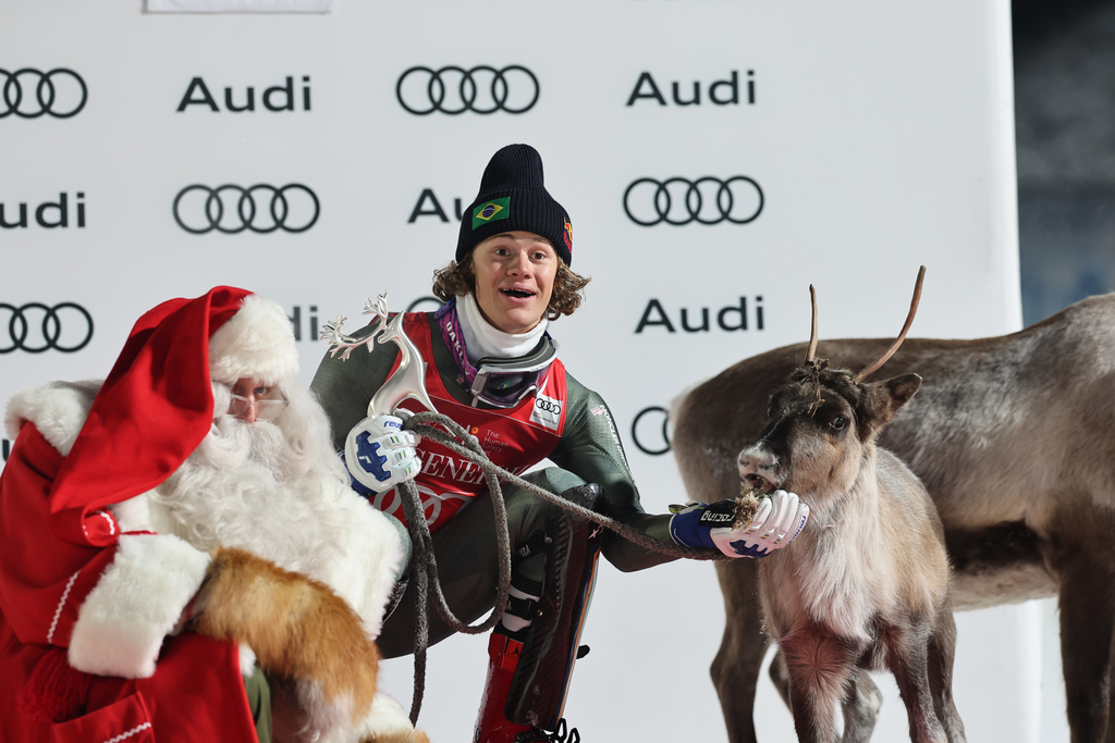 Brazil's Lucas Pinheiro Braathen feeds a deer on the podium after winning an alpine ski, men's World Cup slalom, in Levi, Finland, Sunday, Nov. 16, 2025. (AP Photo/Marco Trovati)