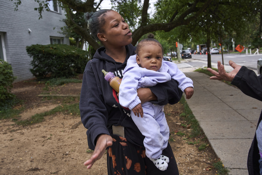 Yanna Stelle, 19, holds her baby Zyanna, 1, as she talks with neighbors in reaction to a large police presence of officers from several federal agencies including Federal Marshalls, Park Police, HSI, and FBI, who arrested a man from within her apartment complex, Tuesday, Aug. 19, 2025, in the Petworth neighborhood of northwest Washington. "That was too many police first thing in the morning," says Stelle, "especially for them just to be doing a warrant. I heard a bunch of walkie talkies and at least 20 officers in the hallways." (AP Photo/Jacquelyn Martin)
