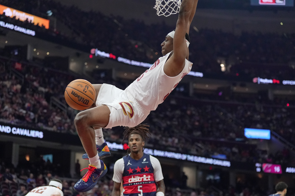 Cleveland Cavaliers forward Nae'qwan Tomlin hangs from the basket after dunking in front of Washington Wizards guard Jamir Watkins (5) in the second half of an NBA basketball game in Cleveland, Sunday, April 12, 2026. (AP Photo/Sue Ogrocki)