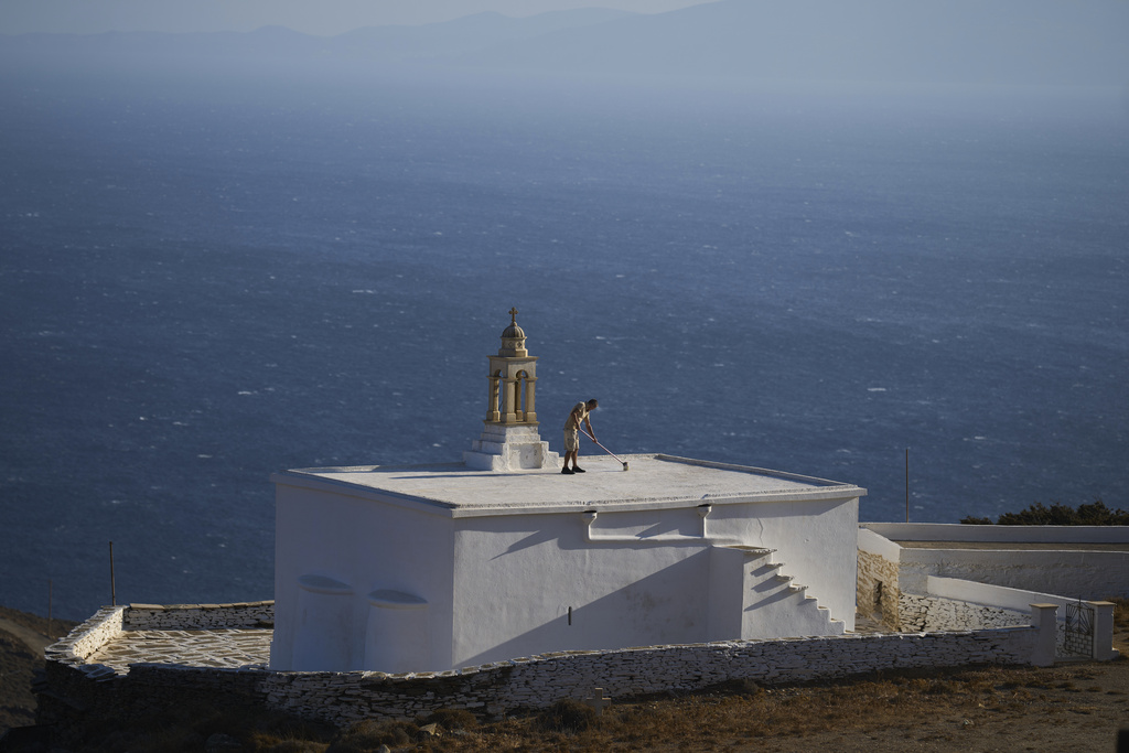 Naim Domi, 50, an Albanian worker who has lived in Greece for 17 years, paints the rooftop of the Panagia Faneromeni family-owned chapel overlooking the Aegean Sea near the village of Pyrgos, on the island of Tinos, Greece, Sunday, Sept. 7, 2025. (AP Photo/Petros Giannakouris)