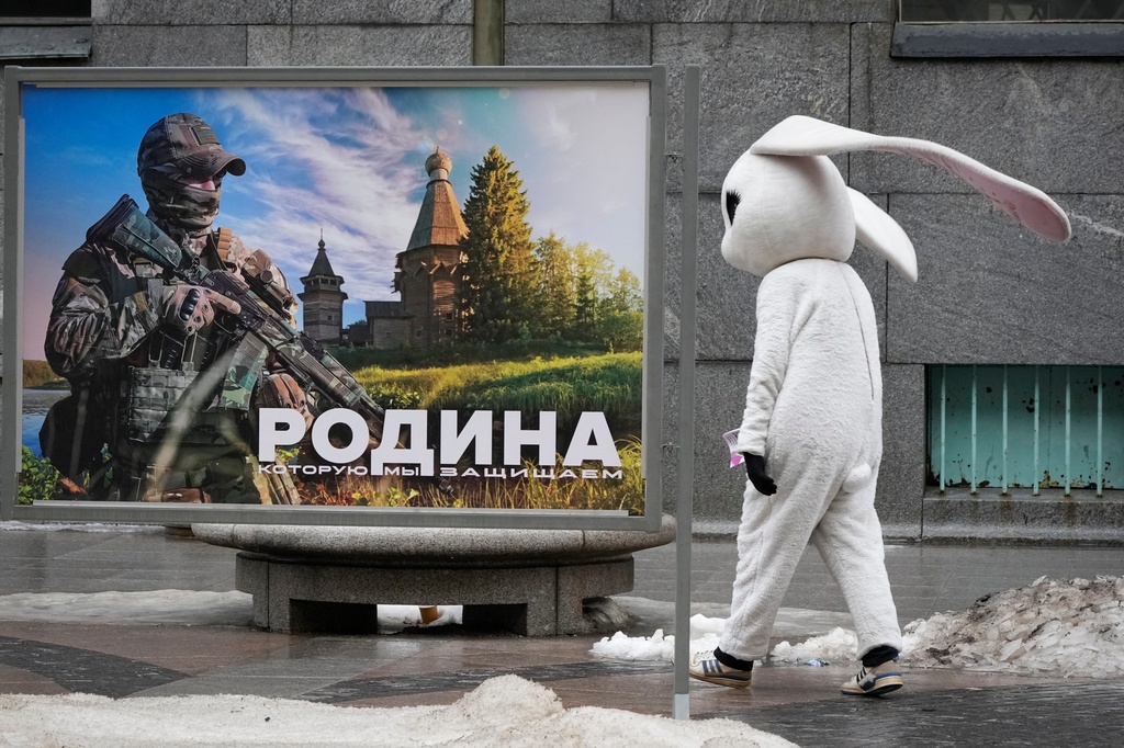 FILE - A street performer walks past a patriotic billboard showing a Russian serviceman and the slogan "The Motherland that we defend" in St. Petersburg, Russia, March 14, 2023. (AP Photo, File)