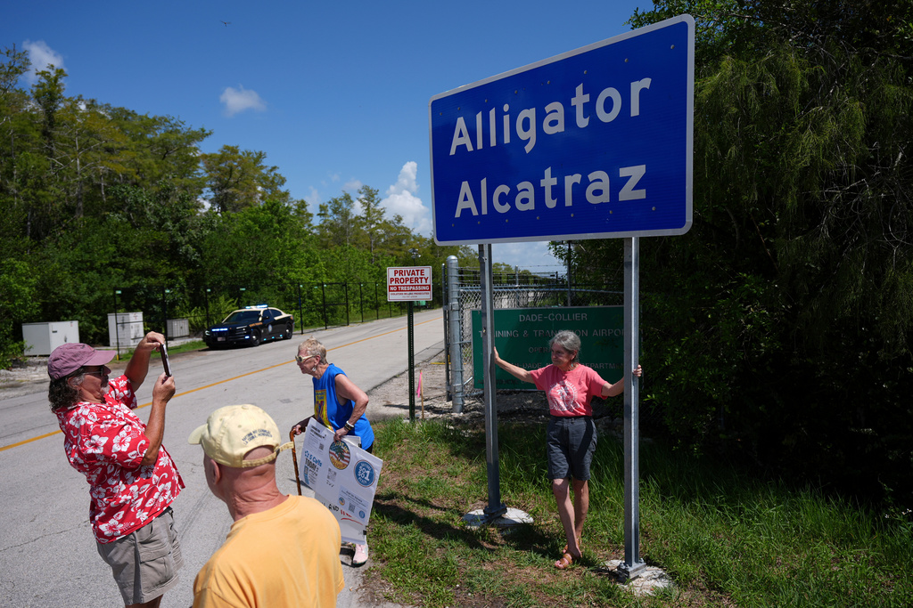 People take pictures in front of a sign reading "Alligator Alcatraz" as passersby, some opposed, some in support, visit the entrance to an immigration detention center in the Florida Everglades, Aug. 28, 2025, in Collier County, Fla. (AP Photo/Rebecca Blackwell, File)