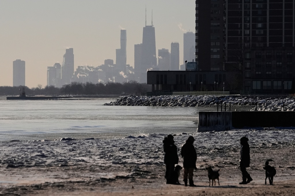 People walk their dogs on an ice covered beach at the Lake Michigan shore, Tuesday, Jan. 20, 2026, in Chicago. (AP Photo/Kiichiro Sato)
