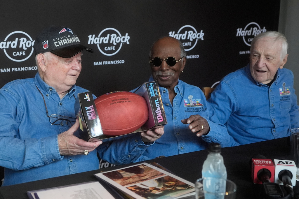 Don Crisman, left, holds up a Super Bowl LX football presented to he and friends Gregory Eaton, middle, and Tom Henschel, who have attended every Super Bowl football game by Wilson Sporting Goods, at a news conference at the Hard Rock Cafe in San Francisco, Friday, Feb. 6, 2026. (AP Photo/Jeff Chiu)