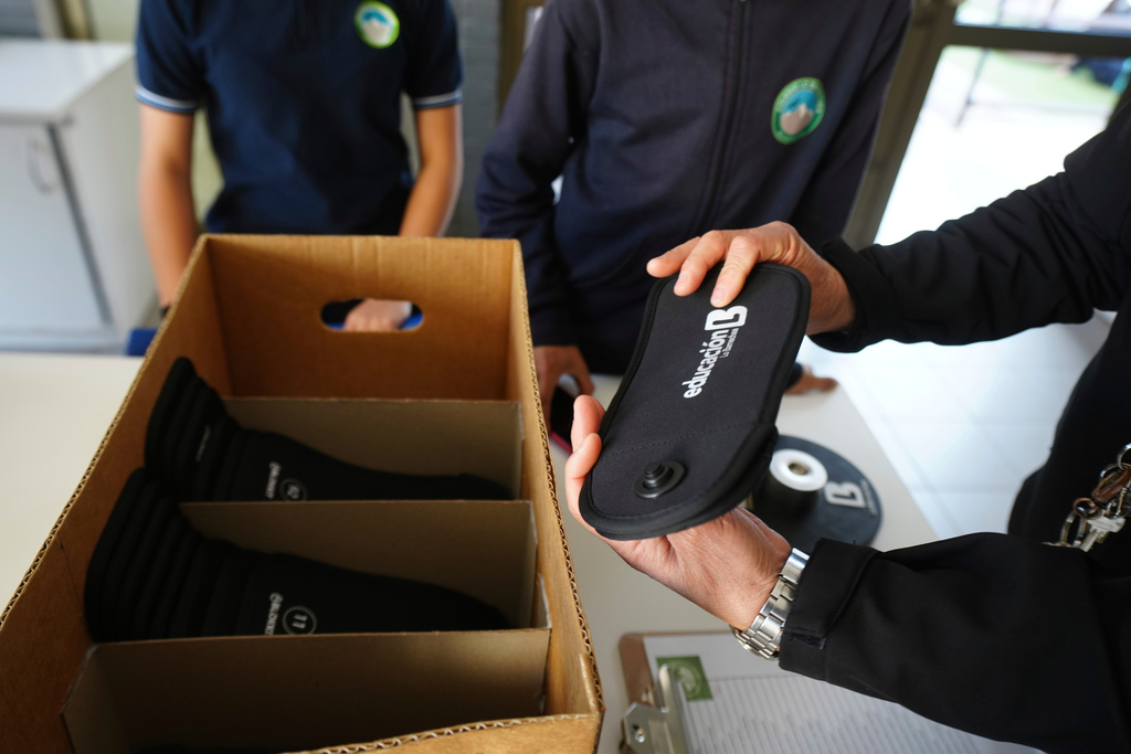 A professor passes out cell phone signal jammers to students to place their cell phones into, as part of a pilot program to reduce mobile use during school hours, at Bicentenario School in Santiago, Chile, Monday, Sept. 8, 2025. (AP Photo/Esteban Felix)