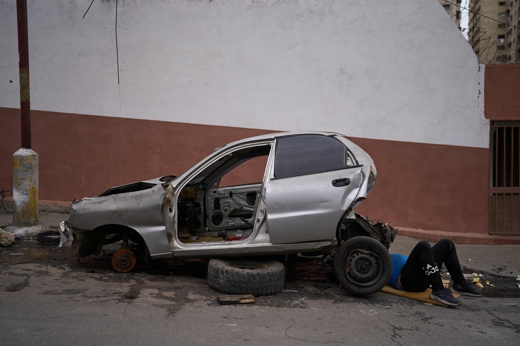 A man works to strip a damaged vehicle of its salvageable components in Caracas, Venezuela, Tuesday, Nov. 11, 2025. (AP Photo/Ariana Cubillos)