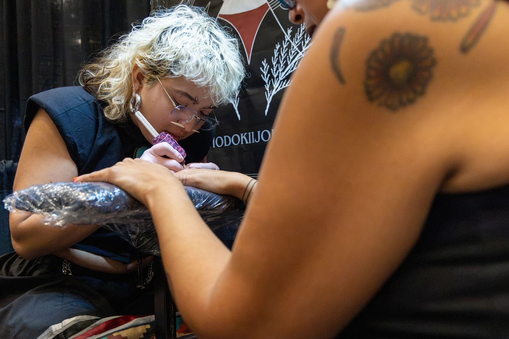 This photo provided by KOSU shows Hodokii Johnson, Muscogee and descendant of the Cheyenne and Arapaho Tribes, holding the hand of Kristin Gentry, Choctaw, as they hand poke three brown lines on each finger on Saturday, Oct. 24, 2026, in Oklahoma City. (Sarah Liese/KOSU via AP)