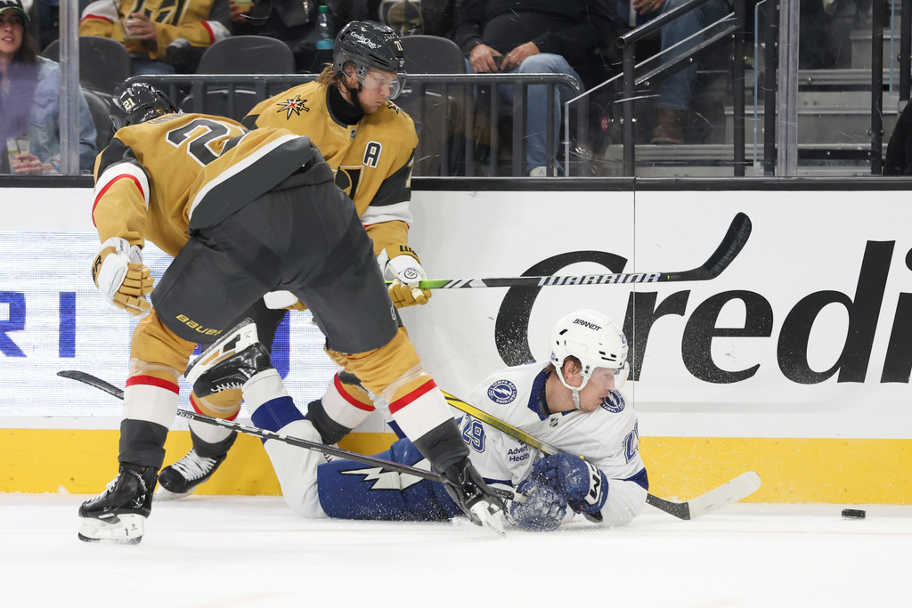 Tampa Bay Lightning right wing Pontus Holmberg, right, falls while being defended by Vegas Golden Knights center Brett Howden (21) and center William Karlsson (71) during the second period of an NHL hockey game Thursday, Nov. 6, 2025, in Las Vegas. (AP Photo/Ian Maule)