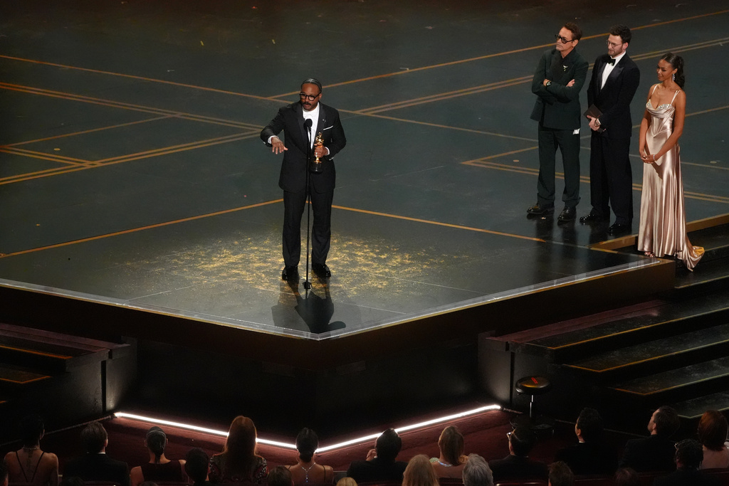 Ryan Coogler accepts the award for writing (original screenplay) for "Sinners" during the Oscars on Sunday, March 15, 2026, at the Dolby Theatre in Los Angeles. Robert Downey Jr., second right, and Chris Evans looks on from right.(AP Photo/Chris Pizzello)