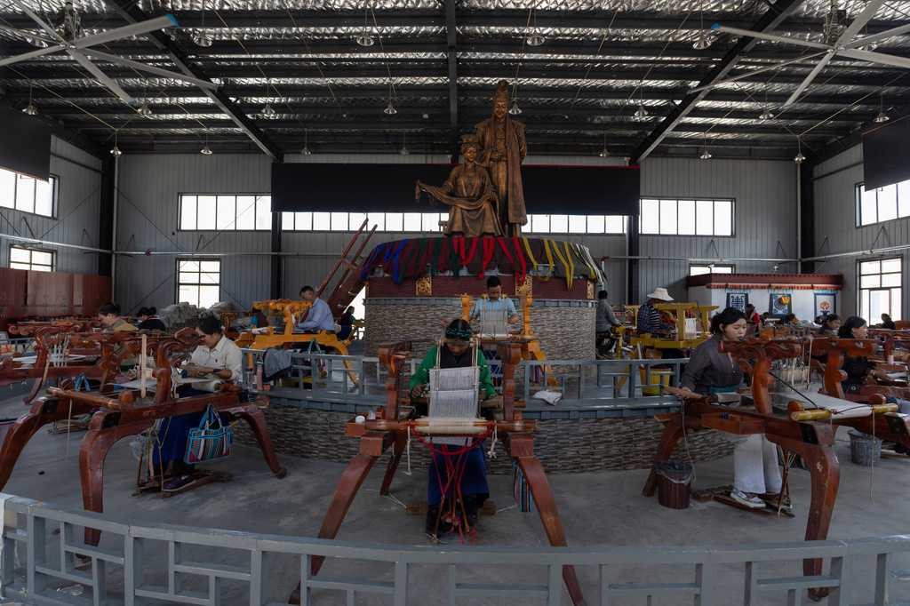Workers weave Pulu, a traditional wooden fabric into clothing, at wooden looms near statues of Princess Wencheng and Tibetan King Songtsen Gampo at the Ethnic Huaji Handwoven Cooperative in Shannan in western China's Tibet Autonomous Region on July 23, 2026, as seen during a government organized visit for foreign journalists. (AP Photo/Ng Han Guan)