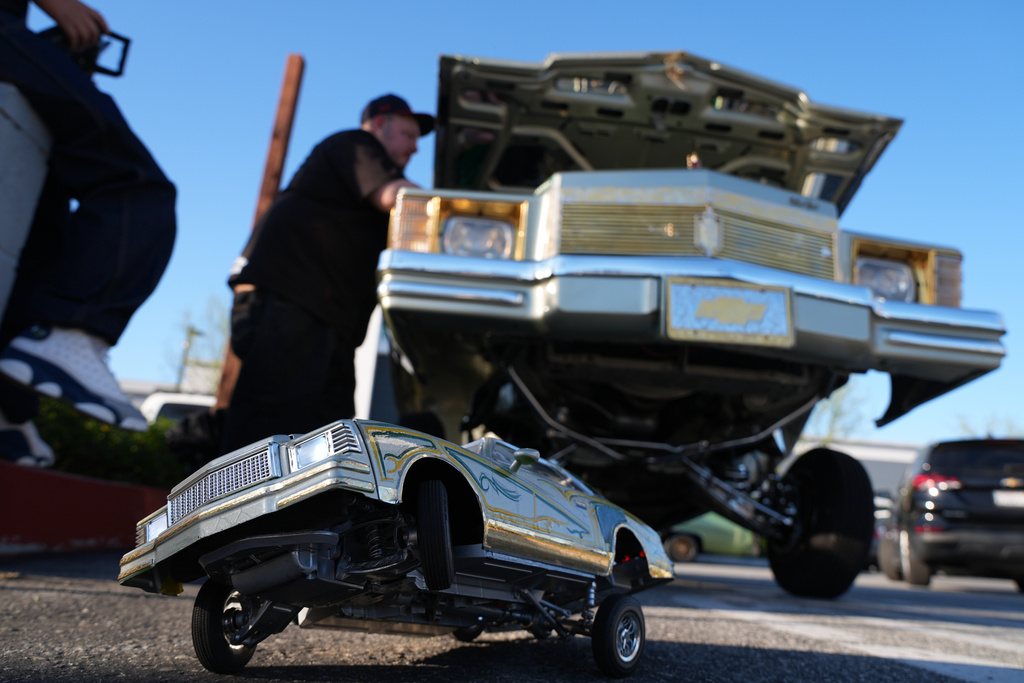 A toy lowrider is placed under a real one at the 6th Annual Lady Lowrider Cruise Night in celebration of International Women's Day in Pasadena, Calif., on Sunday, March 8, 2026. (AP Photo/Damian Dovarganes)
