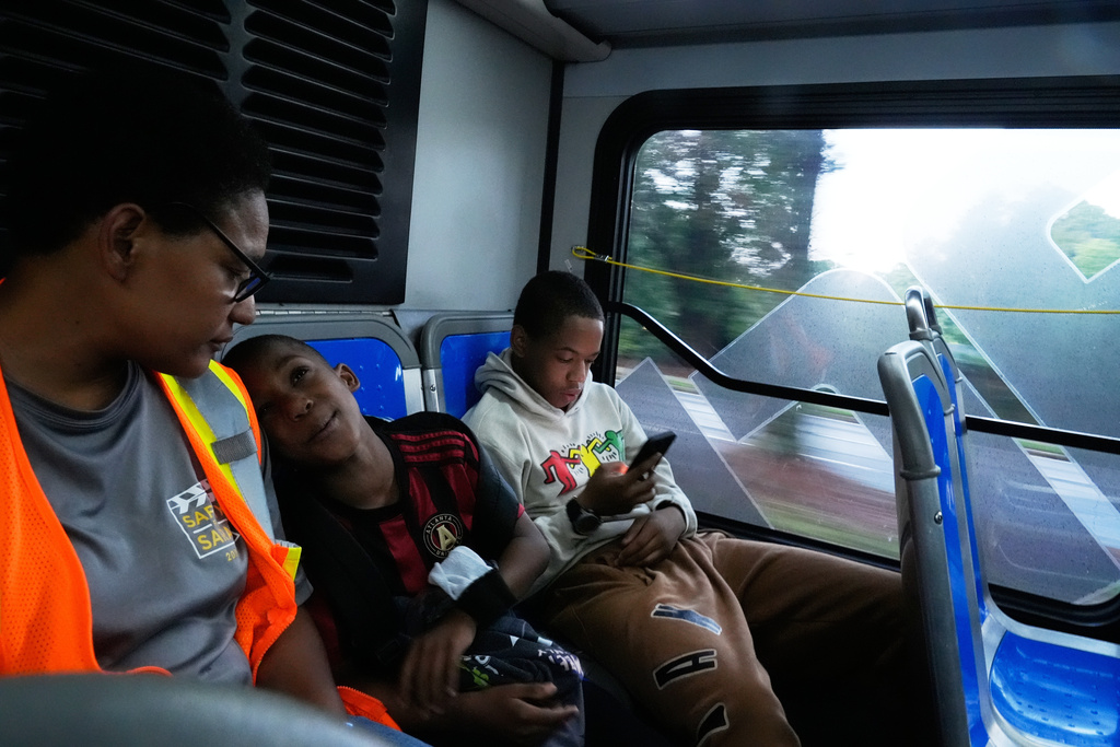 Elias Washington, right, plays on his phone along with his mother Sechita McNair, left, and adopted brother, Derrick McNair-White, center, as they ride the bus to Atlanta on June 11, 2025. (AP Photo/Brynn Anderson)