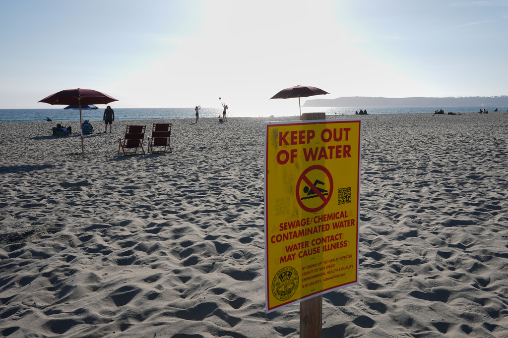 A sign warns of sewage and chemical contaminated water along a beach Tuesday, March 10, 2026, in Coronado, Calif. (AP Photo/Gregory Bull)