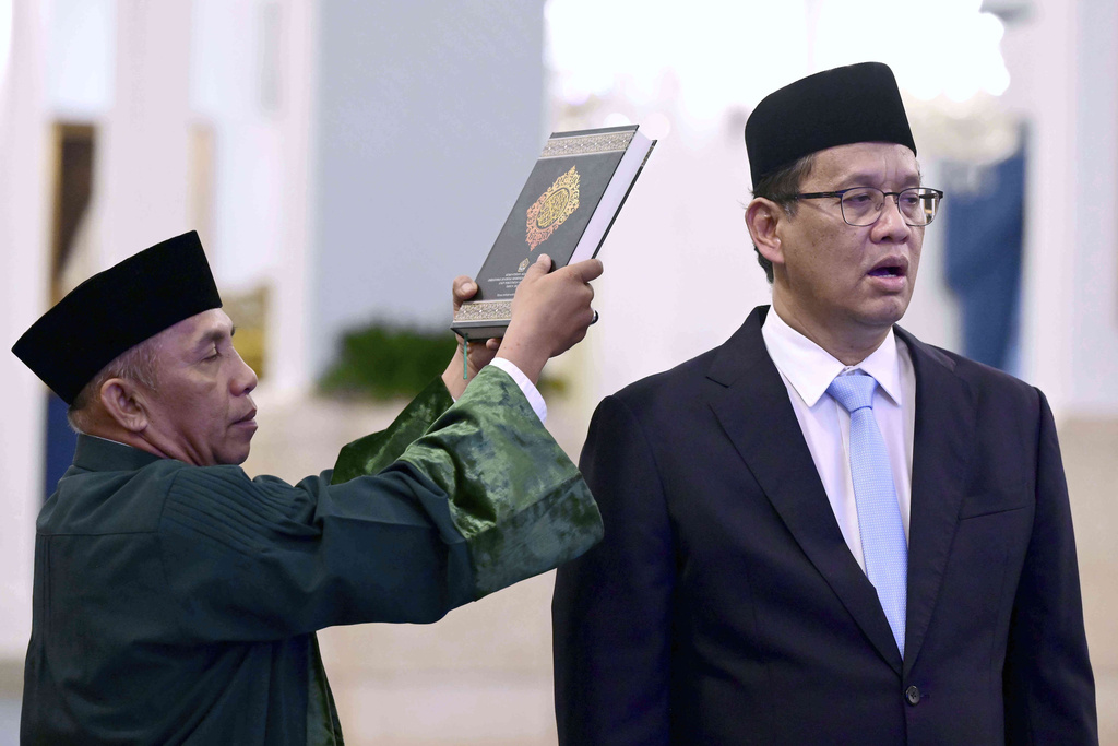 In this photo released by the Press and Media Bureau of the Indonesian Presidential Palace, an Islamic cleric holds a holy book of Quran over the head of newly appointed Finance Minister Purbaya Yudhi Sadewa as he takes his oath during his swearing in ceremony at the State Palace in Jakarta, Indonesia, Monday, Sept. 8, 2025. (Muchlis Jr., Indonesian Presidential Palace via AP)