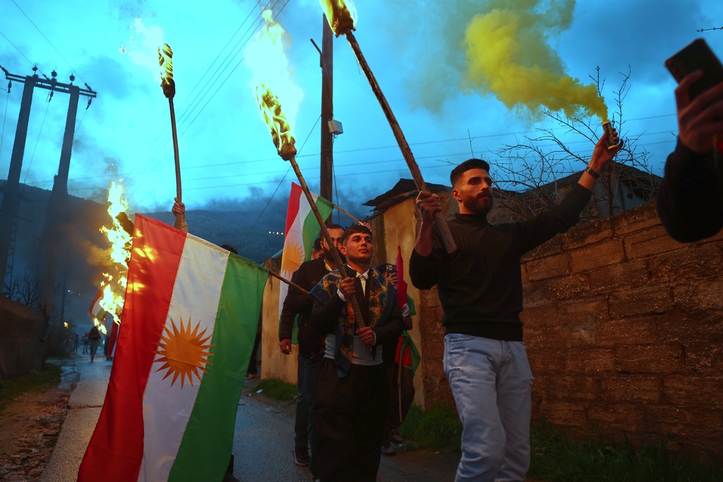 Syrian Kurds hold lit torches and Kurdish flags as they celebrate Nowruz, the Persian New Year, in the village of Basuta in the Afrin countryside, Syria, Friday, March 20, 2026. (AP Photo/Ghaith Alsayed)