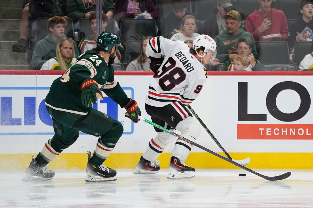 Chicago Blackhawks center Connor Bedard (98) controls the puck as Minnesota Wild defenseman Zach Bogosian (24) challenges during the second period of an NHL hockey preseason game, Sunday, Sept. 28, 2025, in St. Paul, Minn. (AP Photo/Abbie Parr)