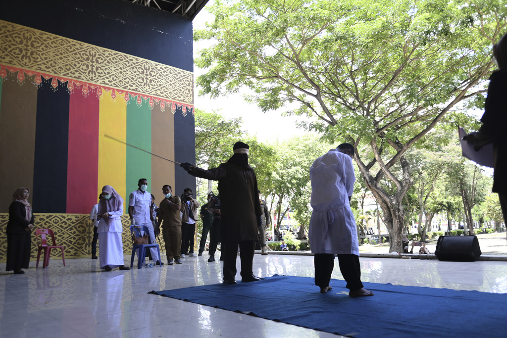 An official uses a rattan cane to whip one of two men convicted of violating Islamic law by hugging and kissing, which the court ruled can lead to banned sexual relations, in Banda Aceh, Aceh province, Indonesia, Tuesday, Aug. 26, 2025. (AP Photo/ Reza Saifullah)