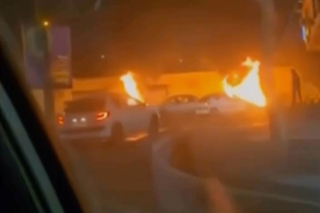 This frame grab from a video released Friday, Jan. 9, 2026, by Iranian state television shows cars driving past burning vehicles during a night of mass protests in Tehran, Iran. (Iranian state TV via AP)