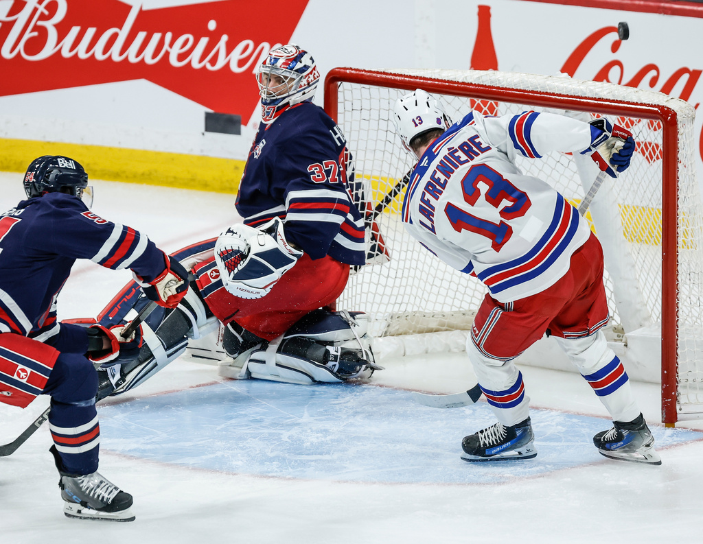 New York Rangers' Alexis Lafreniere's (13) shot just goes over the net behind Winnipeg Jets goaltender Connor Hellebuyck's (37) as Dylan Samberg (54) defends during the first period of an NHL game in Winnipeg, Thursday, March 12, 2026. (John Woods/The Canadian Press via AP)