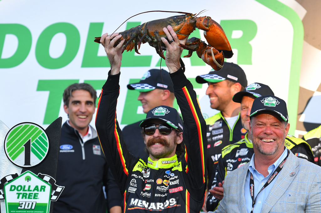 Ryan Blaney, center front, displays a lobster, a Victory Lane tradition at New Hampshire Motor Speedway, after winning a NASCAR Cup Series auto race, Sunday, Aug. 23, 2026, at the speedway in Loudon, N.H., as David McGrath, right, executive vice president and general manager of the speedway looks on. (AP Photo/Steven Senne)