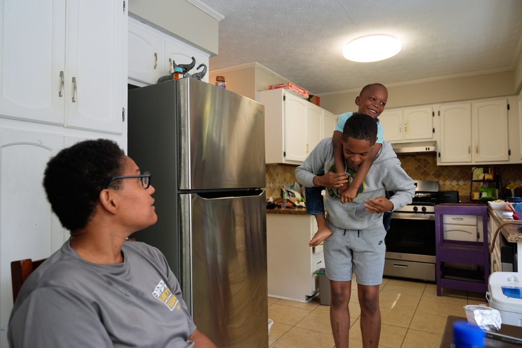 Elias Washington holds Malachi McNair-Nesbitt in the kitchen with their mother, Sechita McNair, left, on June 7, 2025, in Jonesboro, Ga. (AP Photo/Brynn Anderson)