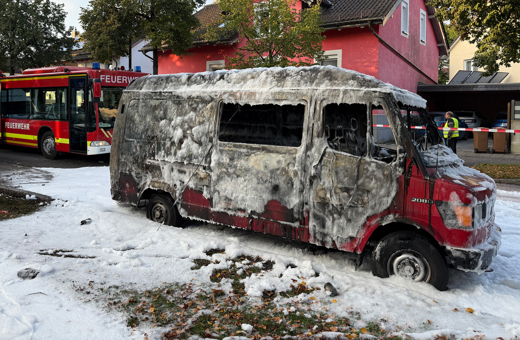 A burned van is covered by extinguishing foam after a fire in Munich, Germany, Wednesday, Oct. 1, 2025. (Roland Freund/dpa via AP)