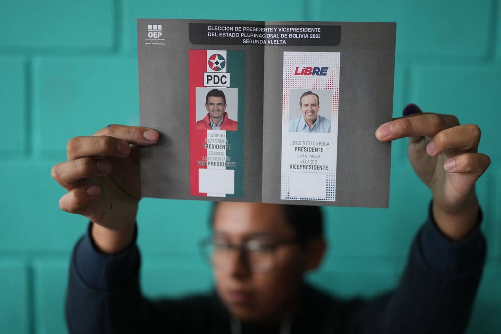 An electoral official shows an unmarked ballot with presidential candidates Jorge Quiroga, right, and Rodrigo Paz to voters during a runoff election in La Paz, Bolivia, Sunday, Oct. 19, 2025. (AP Photo/Natacha Pisarenko)