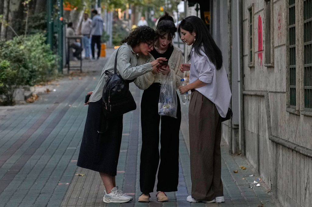 Women check their smartphone on a sidewalk in northern Tehran, Iran, Thursday, Aug. 13, 2026. (AP Photo/Vahid Salemi)