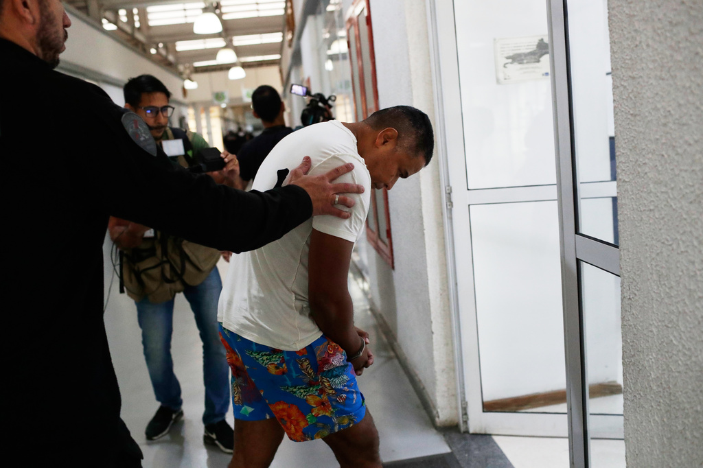 A suspected member of the criminal group Comando Vermelho, or Red Command, is lead in handcuffs by a police officer into a police station in Rio de Janeiro, Friday, May 29, 2026. (AP Photo/Bruna Prado)