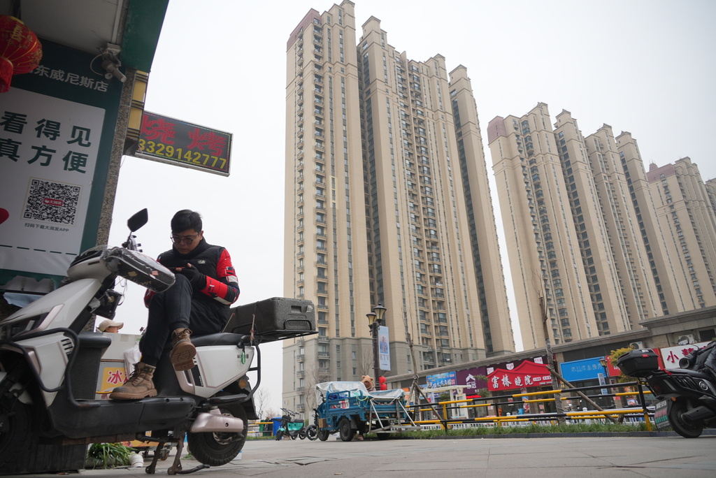 A delivery driver idles away time by watching videos on his phone on his scooter in the semi-abandoned "Life in Venice" housing complex in Qidong, on China's east coast, Feb. 5, 2026. (AP Photo/Dake Kang)